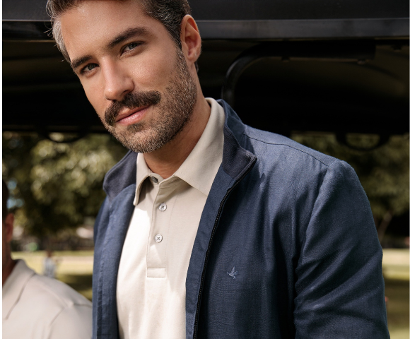 Homem estiloso com barba, usando jaqueta azul e camisa branca que combinam com a tendência de moda masculina, em ambiente ao ar livre.